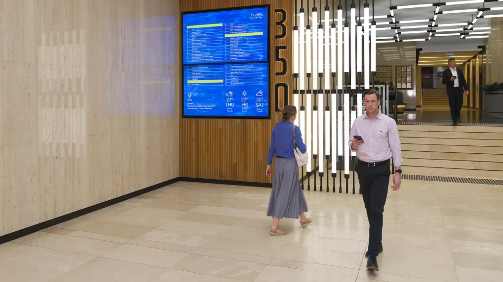 Multi-Screen Digital Tenant Directory in the busy marble lined foyer of 350 Collins Street. Image shows office workers passing by the large Tenant Directory on the wall.